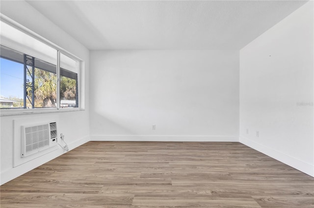 unfurnished room with a wall mounted air conditioner, baseboards, and light wood finished floors