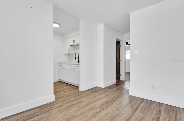 spare room with light wood finished floors, a sink, and baseboards