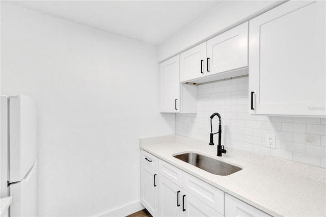 kitchen featuring a sink, white cabinetry, decorative backsplash, freestanding refrigerator, and light stone countertops