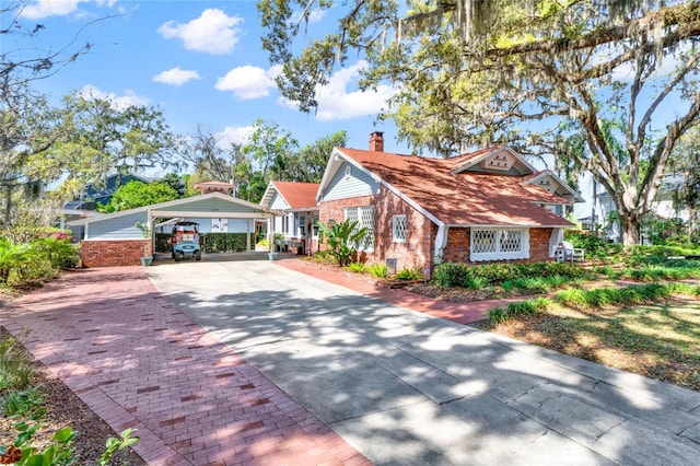 view of front facade featuring a carport, a chimney, decorative driveway, and brick siding