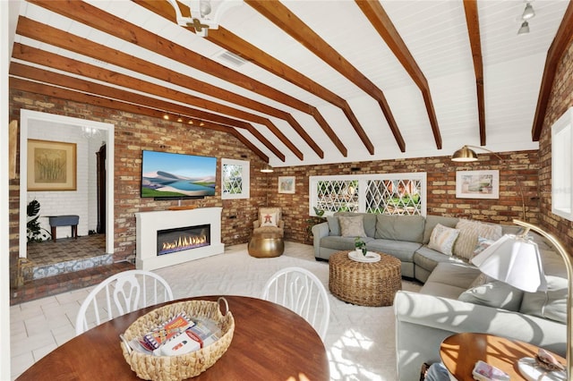 tiled living area with vaulted ceiling with beams, brick wall, and a glass covered fireplace