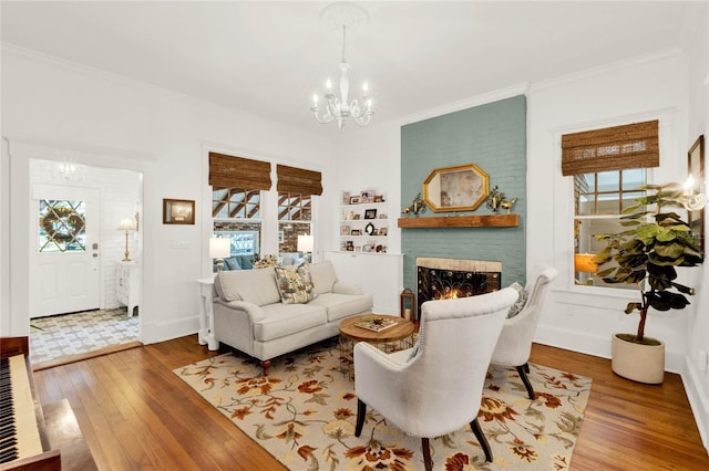 living area featuring hardwood / wood-style flooring, baseboards, ornamental molding, a brick fireplace, and an inviting chandelier