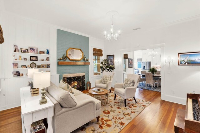 living area with a notable chandelier, baseboards, a brick fireplace, wood-type flooring, and crown molding