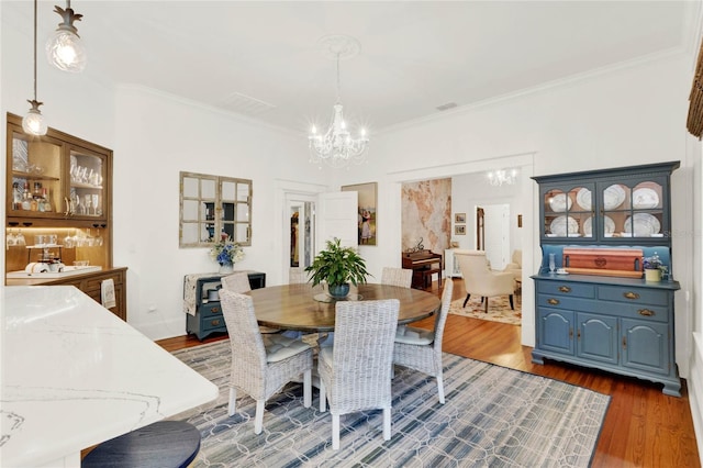 dining room with crown molding, wood finished floors, visible vents, and an inviting chandelier