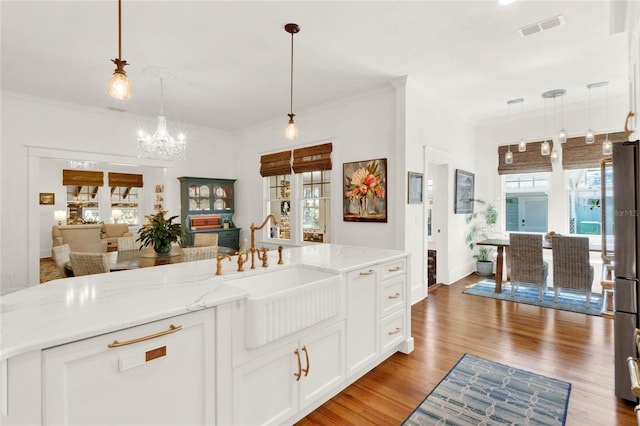 kitchen with visible vents, white cabinets, a sink, light wood-style floors, and a notable chandelier