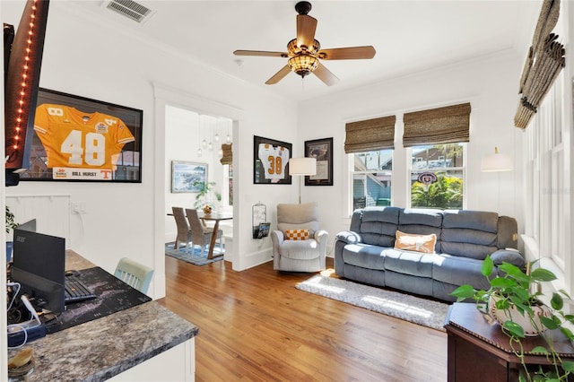 living area with light wood-style floors, visible vents, ornamental molding, and ceiling fan