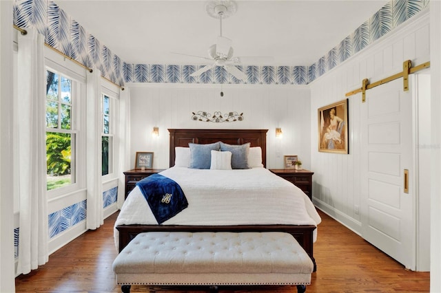 bedroom featuring a ceiling fan, a barn door, baseboards, and wood finished floors