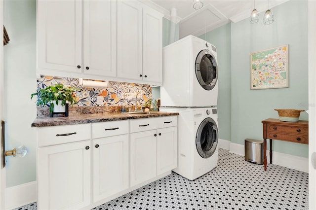 washroom with cabinet space, attic access, baseboards, stacked washing maching and dryer, and a sink