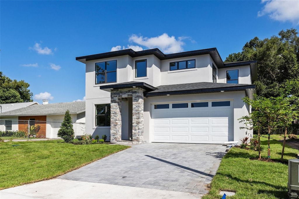 prairie-style house with an attached garage, stone siding, decorative driveway, stucco siding, and a front lawn