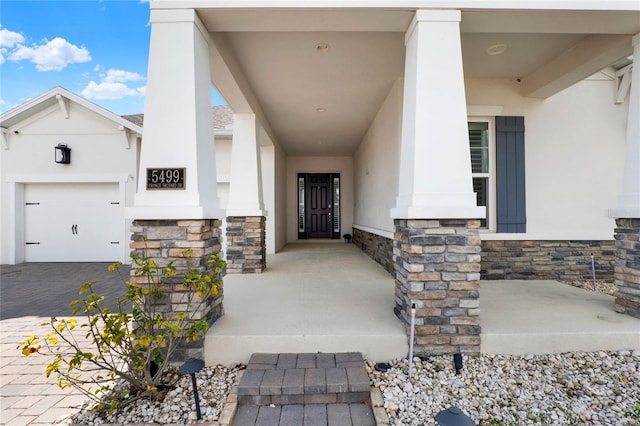 view of exterior entry featuring decorative driveway, stucco siding, a porch, a garage, and stone siding