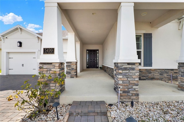 entrance to property with a garage, stone siding, decorative driveway, and stucco siding