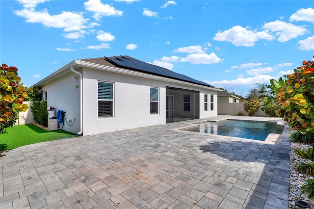 back of property with a patio, stucco siding, roof mounted solar panels, a fenced backyard, and an outdoor pool