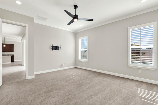 spare room with light carpet, visible vents, baseboards, a ceiling fan, and crown molding