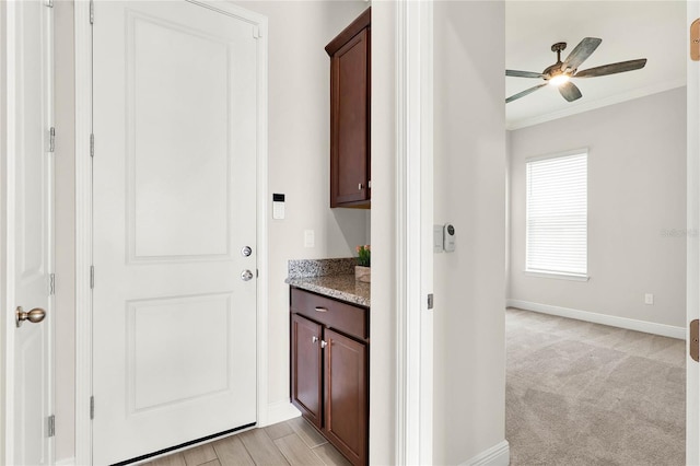 corridor with ornamental molding, light colored carpet, and baseboards