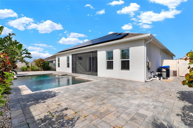 back of property with a fenced in pool, a patio, a gate, roof mounted solar panels, and stucco siding