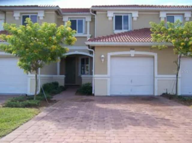 view of front facade featuring a garage, a tile roof, and decorative driveway