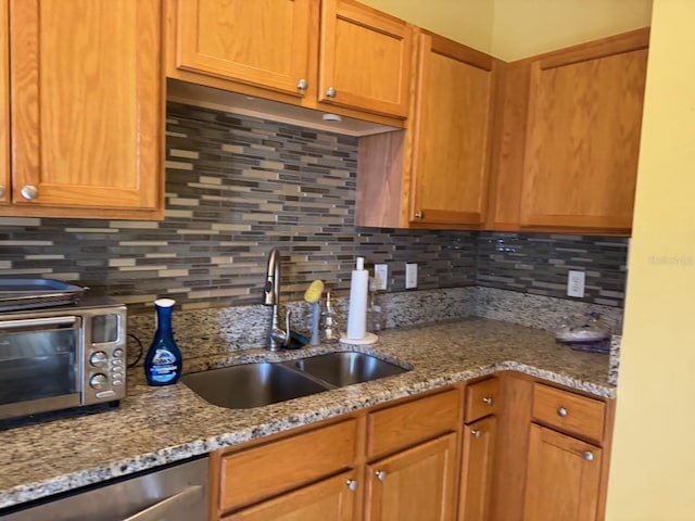 kitchen with decorative backsplash, brown cabinetry, a sink, light stone countertops, and dishwasher