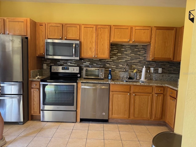 kitchen featuring light tile patterned floors, light stone counters, stainless steel appliances, and a sink