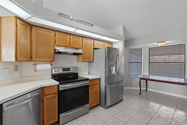 kitchen featuring light countertops, backsplash, appliances with stainless steel finishes, vaulted ceiling, and under cabinet range hood