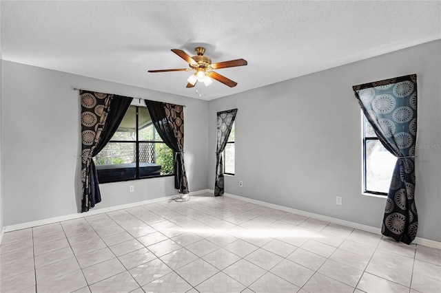 spare room with ceiling fan, a textured ceiling, baseboards, and light tile patterned floors