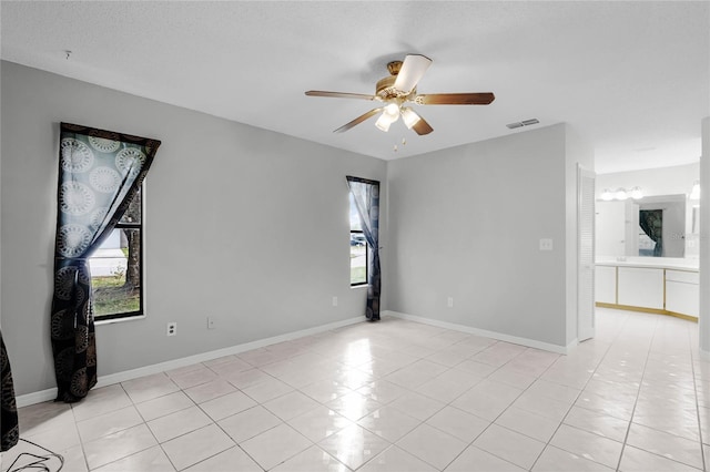 empty room with light tile patterned flooring, ceiling fan, visible vents, and baseboards