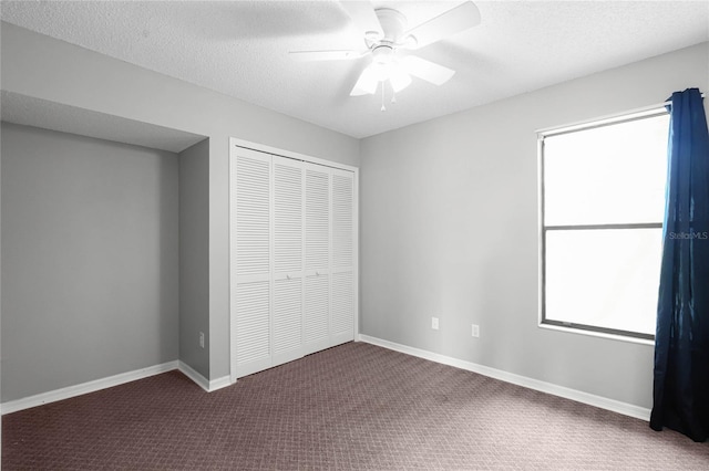 unfurnished bedroom with a closet, dark carpet, a textured ceiling, and baseboards