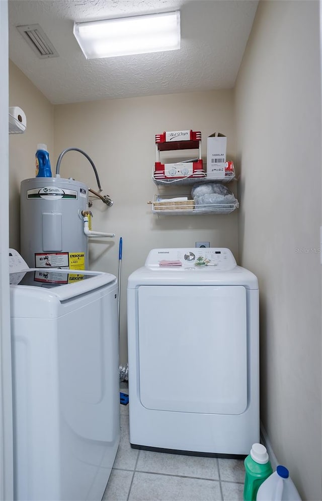 laundry area with light tile patterned floors, electric water heater, laundry area, visible vents, and washing machine and clothes dryer