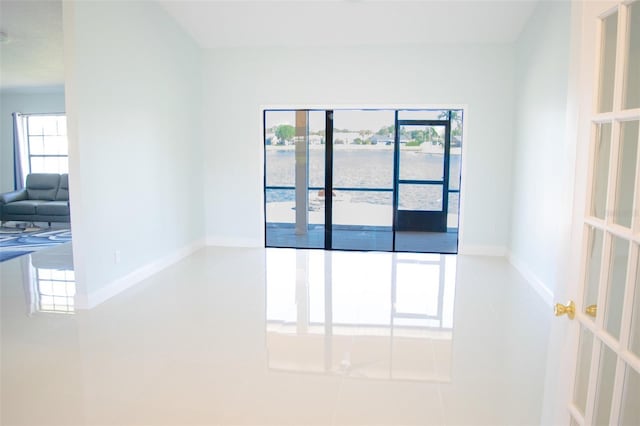 tiled empty room featuring a water view and baseboards