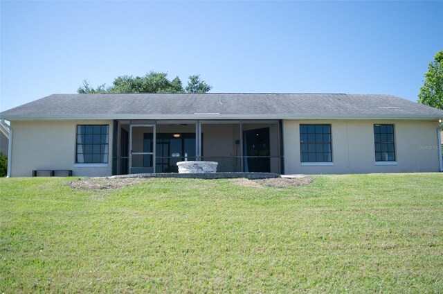 back of property with a yard, roof with shingles, a sunroom, and stucco siding