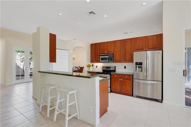 kitchen featuring arched walkways, stainless steel appliances, recessed lighting, dark stone counters, and a kitchen breakfast bar