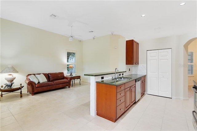 kitchen with arched walkways, stainless steel appliances, a sink, open floor plan, and brown cabinetry