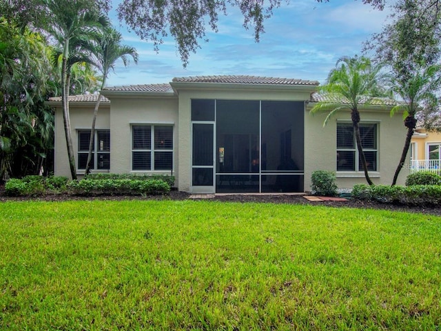 back of house featuring a sunroom, a yard, a tiled roof, and stucco siding