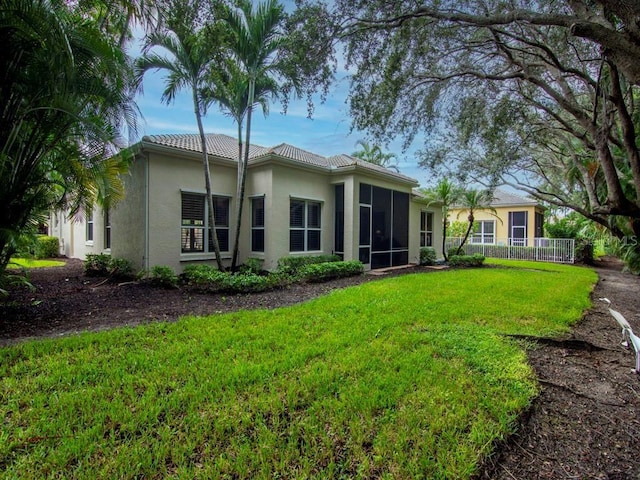 rear view of property with a tile roof, stucco siding, a lawn, a sunroom, and fence