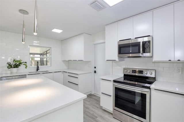 kitchen with stainless steel appliances, tasteful backsplash, visible vents, white cabinets, and a sink