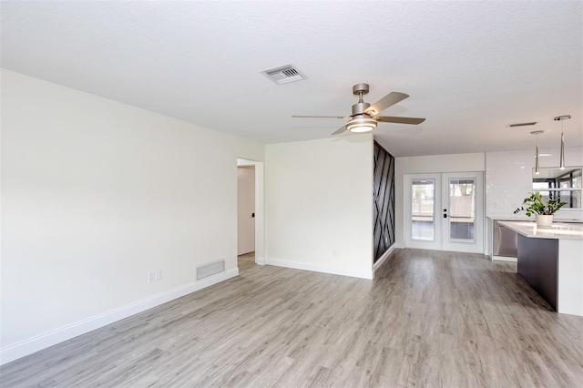 unfurnished living room with baseboards, french doors, visible vents, and light wood-style floors