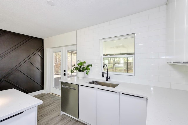 kitchen featuring white cabinets, dishwasher, light countertops, light wood-type flooring, and a sink