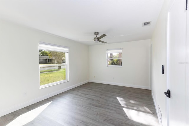 empty room with baseboards, wood finished floors, visible vents, and a healthy amount of sunlight