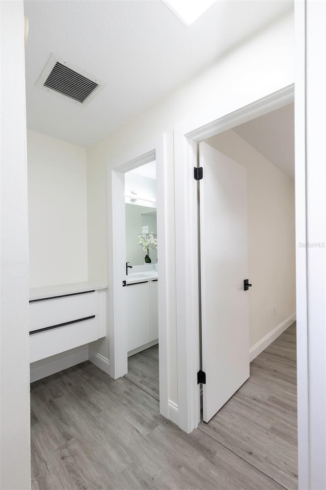 hallway with light wood-style floors, baseboards, and visible vents