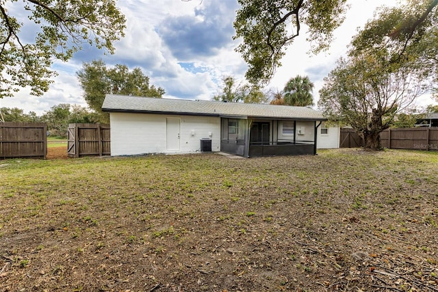 rear view of property with central air condition unit, a sunroom, a fenced backyard, and a lawn