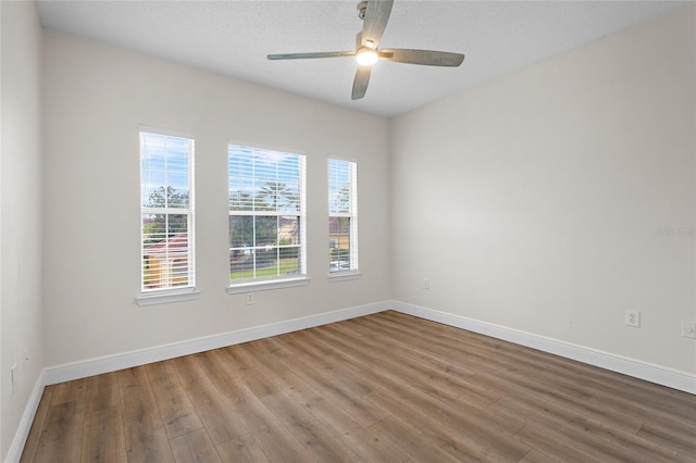 spare room with wood finished floors, a ceiling fan, and baseboards