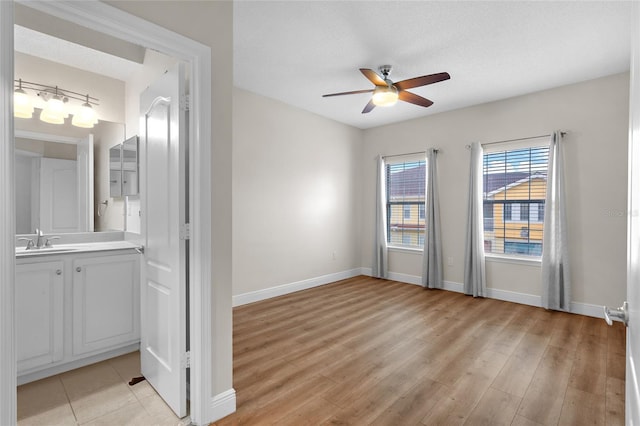 spare room featuring a textured ceiling, light wood-style flooring, a sink, a ceiling fan, and baseboards