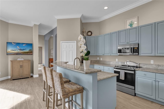 kitchen with appliances with stainless steel finishes, arched walkways, crown molding, and a kitchen bar