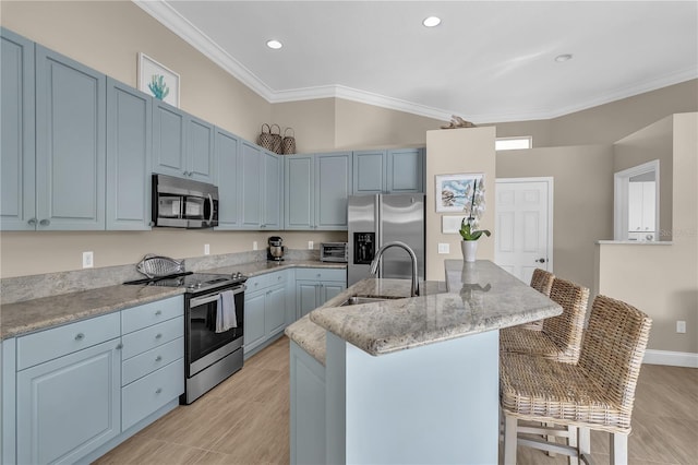 kitchen with a center island with sink, a breakfast bar area, stainless steel appliances, crown molding, and a sink