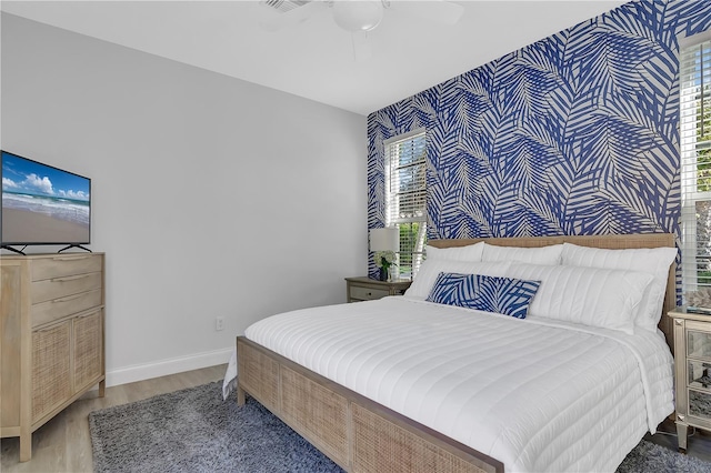 bedroom featuring an accent wall, a ceiling fan, baseboards, and wood finished floors