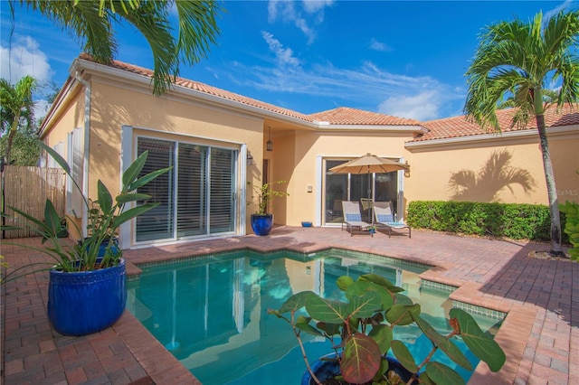 rear view of property with a tile roof, a patio, stucco siding, fence, and an outdoor pool