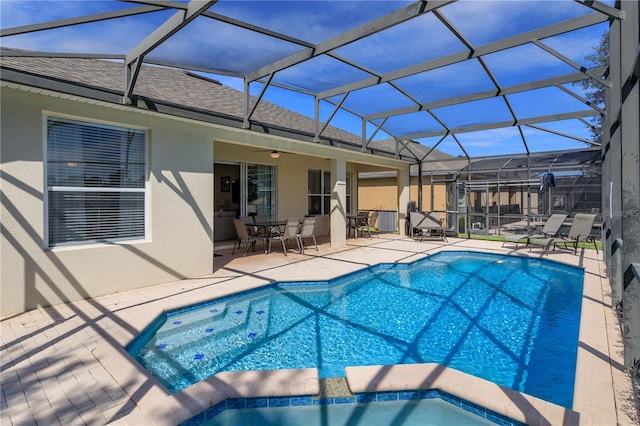 view of pool with outdoor dining area, a patio, a pool with connected hot tub, a ceiling fan, and glass enclosure