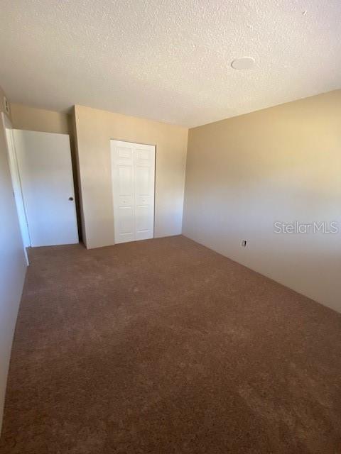 unfurnished bedroom with carpet, a textured ceiling, and a closet