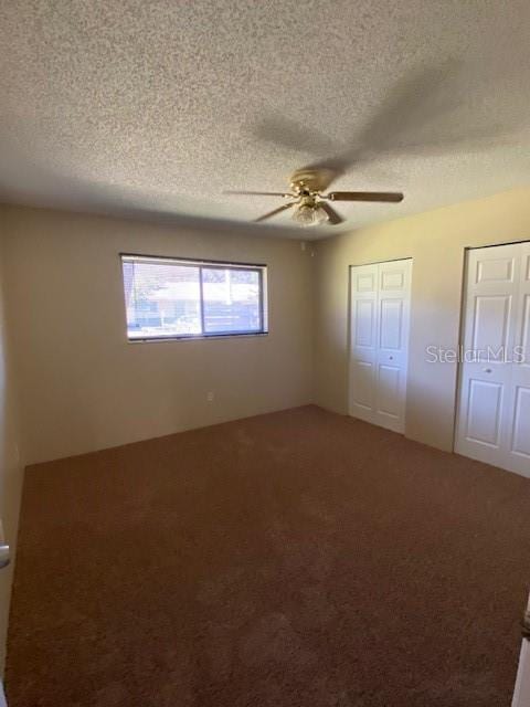 unfurnished bedroom featuring a ceiling fan, carpet flooring, a textured ceiling, and two closets