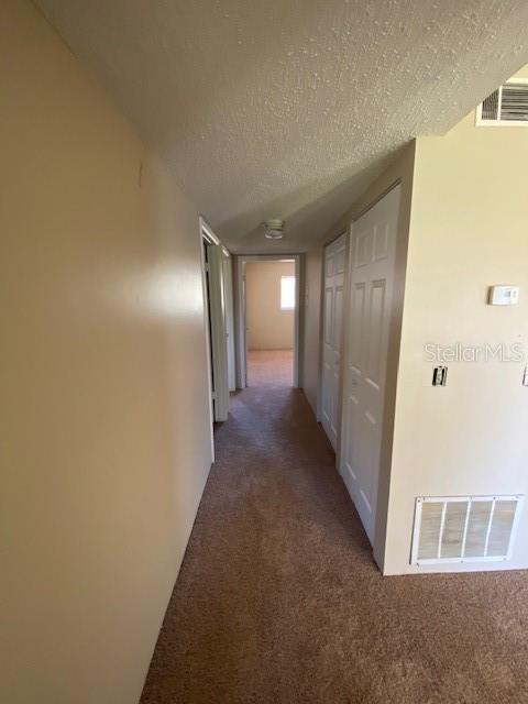 hall with visible vents, dark carpet, and a textured ceiling