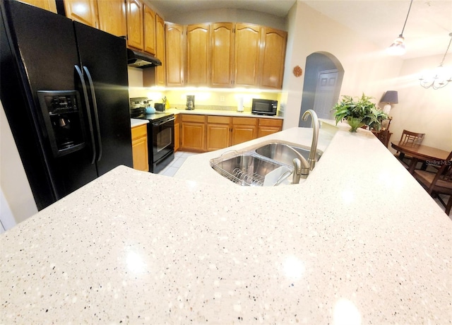 kitchen featuring arched walkways, under cabinet range hood, a sink, hanging light fixtures, and black appliances